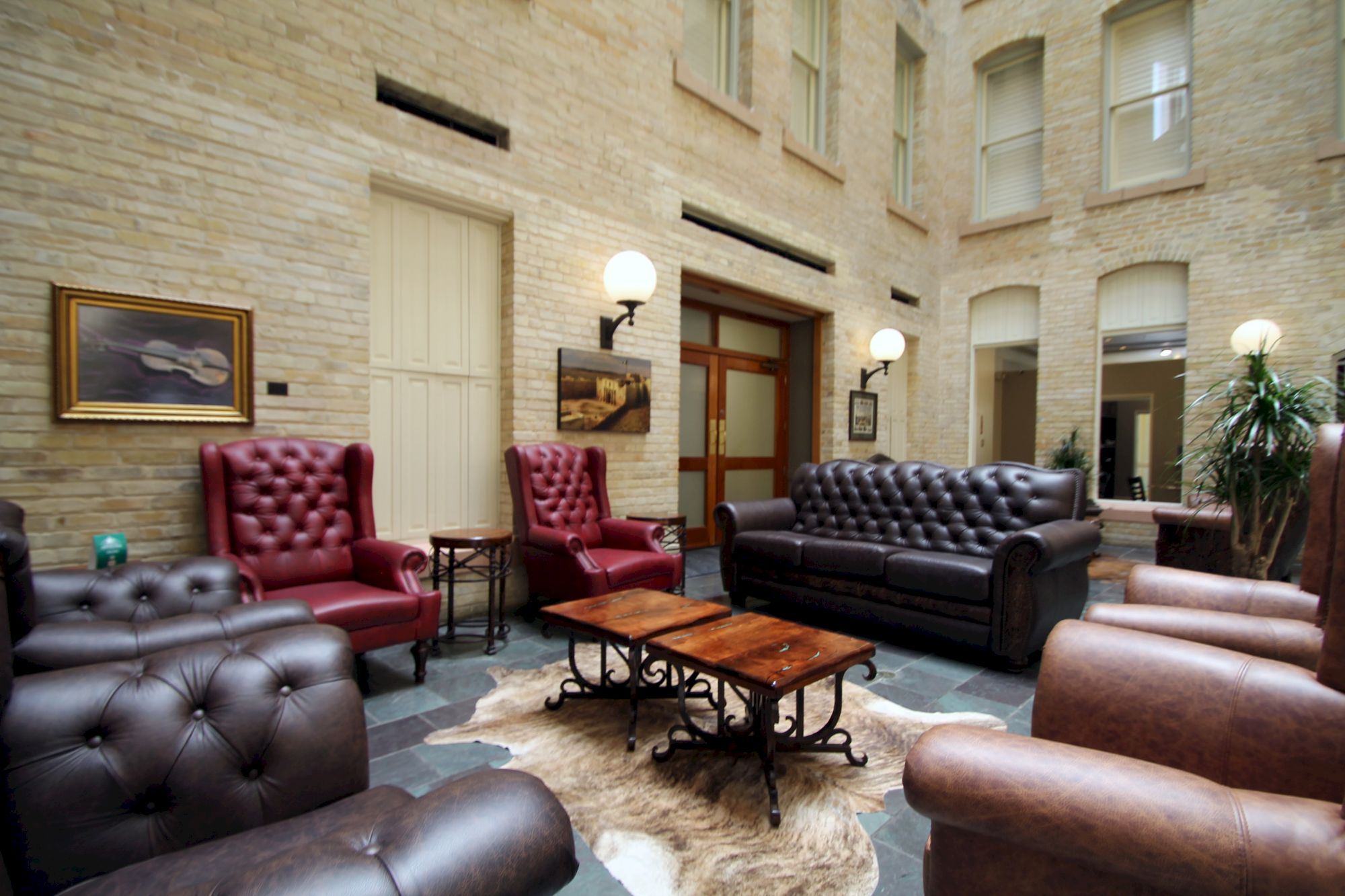 Luxurious lounge with leather tufted chairs and sofas, wooden coffee table, warm lamps, and classic decor in a brick-walled indoor courtyard.