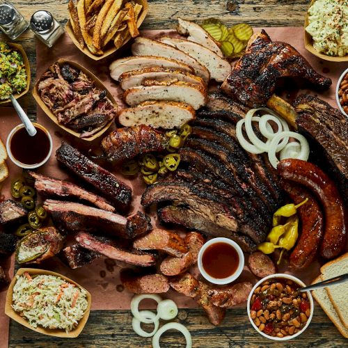 A big spread of barbecue meats, sausages, ribs, and sides, plus bread, pickles, onions, dips, and condiments.