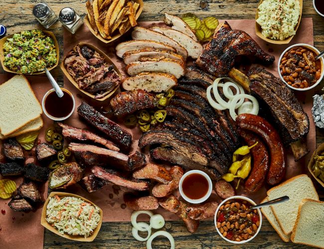 A big spread of barbecue meats, sausages, ribs, and sides, plus bread, pickles, onions, dips, and condiments.
