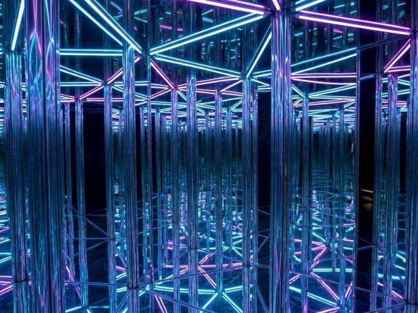 A maze of mirrored steel tubes glowing in blue and pink neon, creating infinite reflections and a futuristic, kaleidoscopic tunnel.