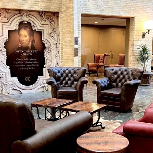 A stylish lounge with brown leather seating, red chairs, and round wooden tables, set in a cozy hotel lobby with warm lighting and ornate decor.
