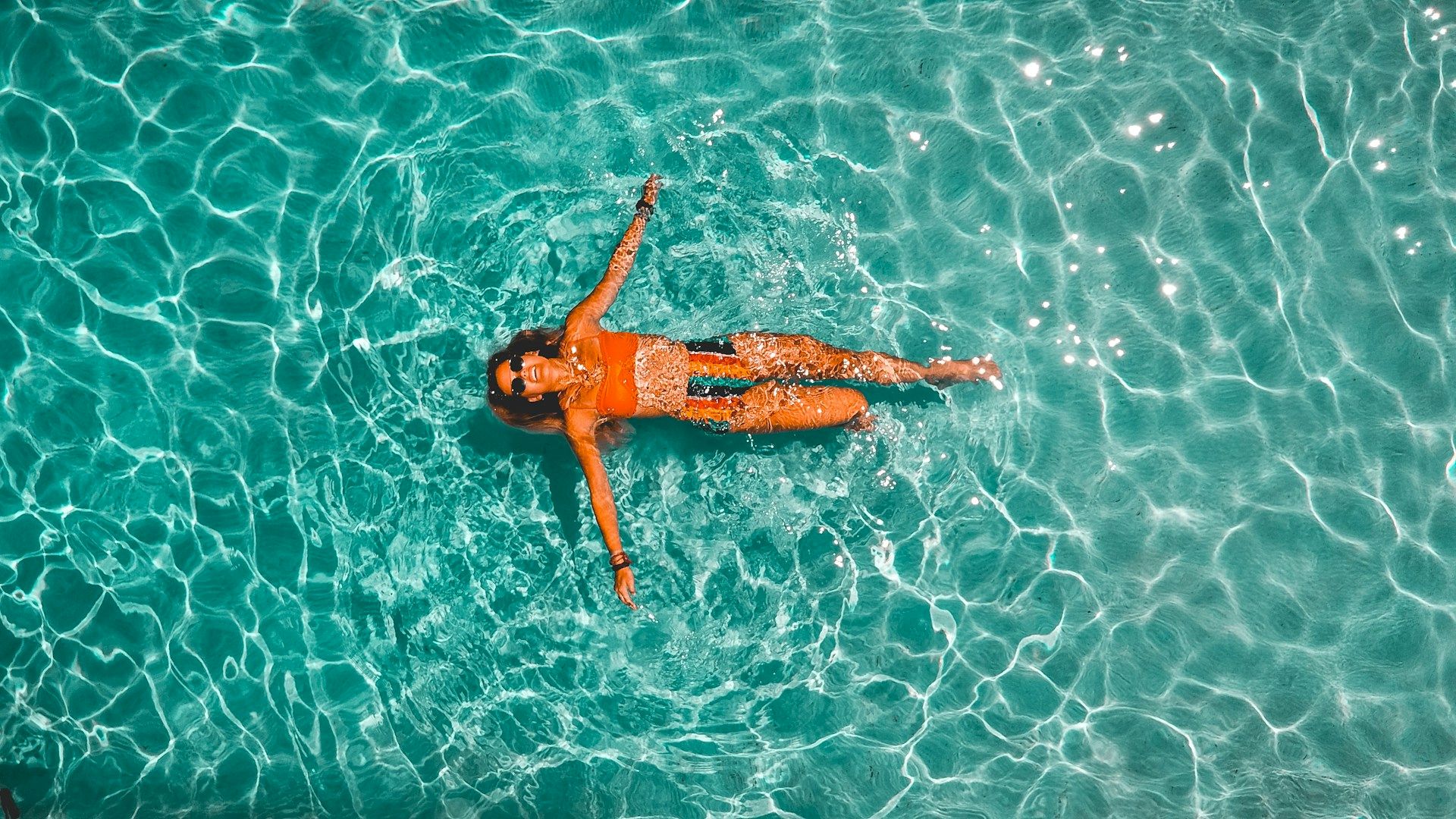 A swimmer floating on their back in clear turquoise ocean water, arms out, creating ripples and bubbles.