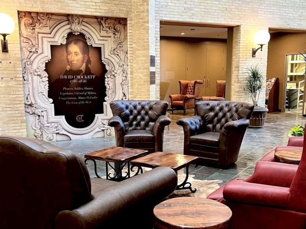 Luxurious hotel lobby with tufted leather chairs, wooden tables, warm lighting, and a decorative doorway featuring a framed portrait.