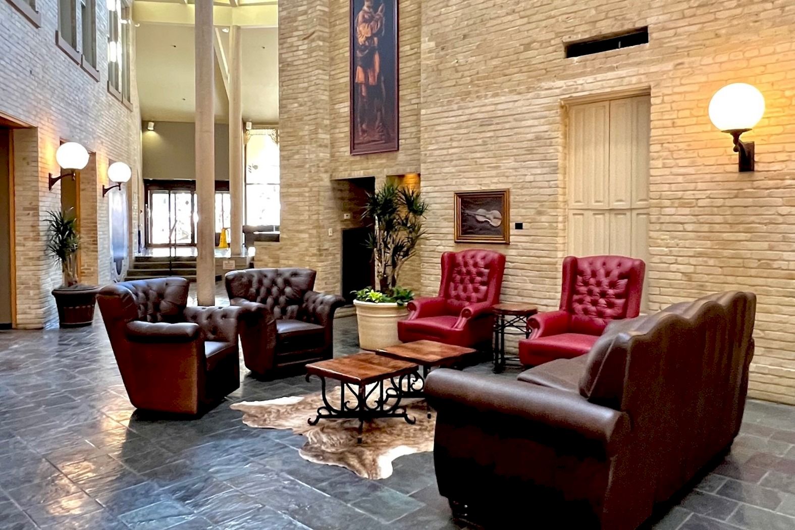 A cozy lounge area with red and brown tufted chairs, a coffee table, potted plants, and a brick wall fireplace.